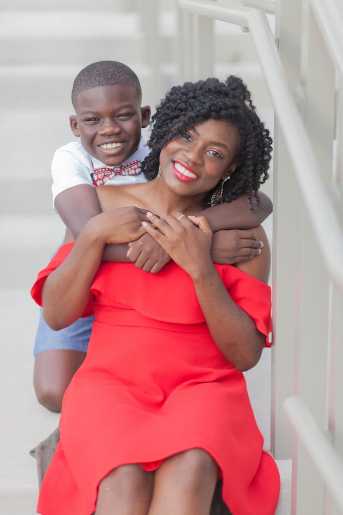 A cheerful African American mother and son share a loving hug on a staircase, both smiling brightly.