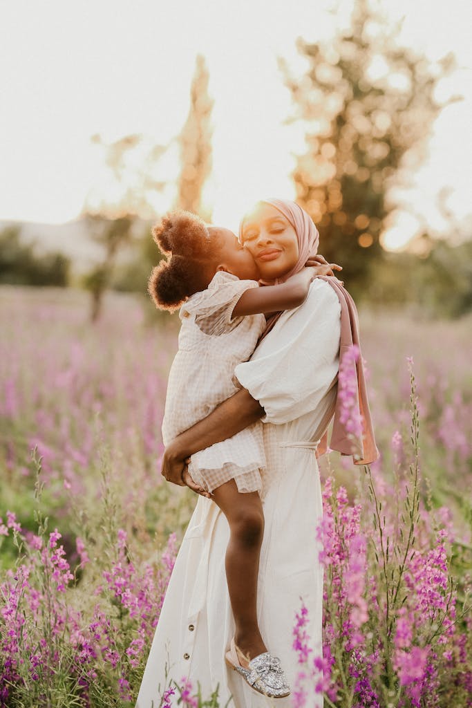 Mother and child in a loving embrace surrounded by blooming flowers in a summer meadow.