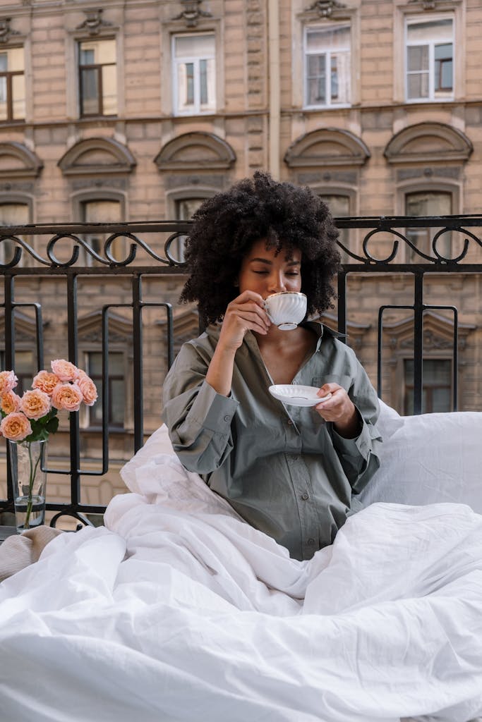 Pregnant woman sipping coffee on a cozy balcony, surrounded by flowers.