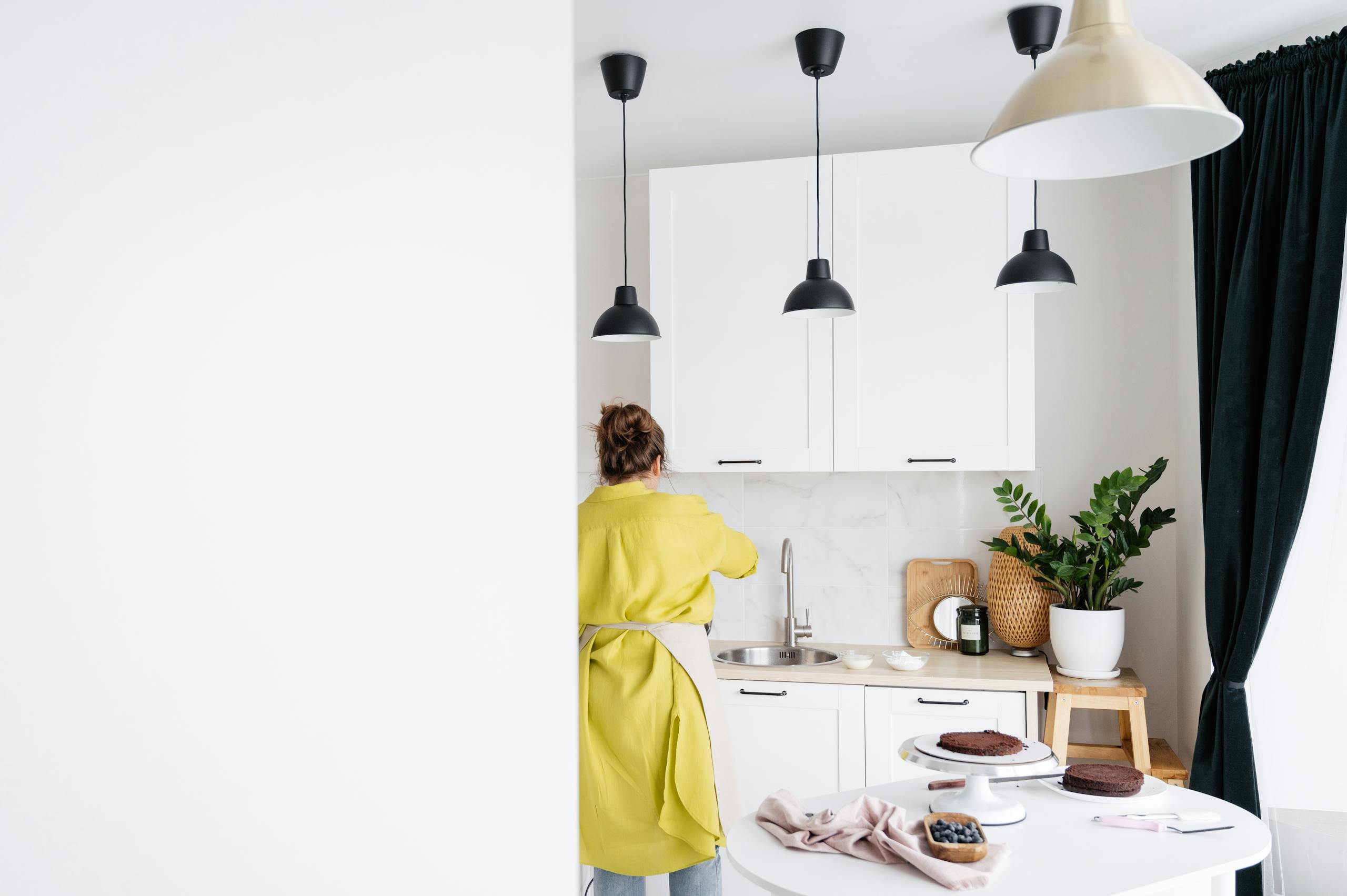 Woman in yellow apron baking desserts in a modern kitchen with white cabinets.